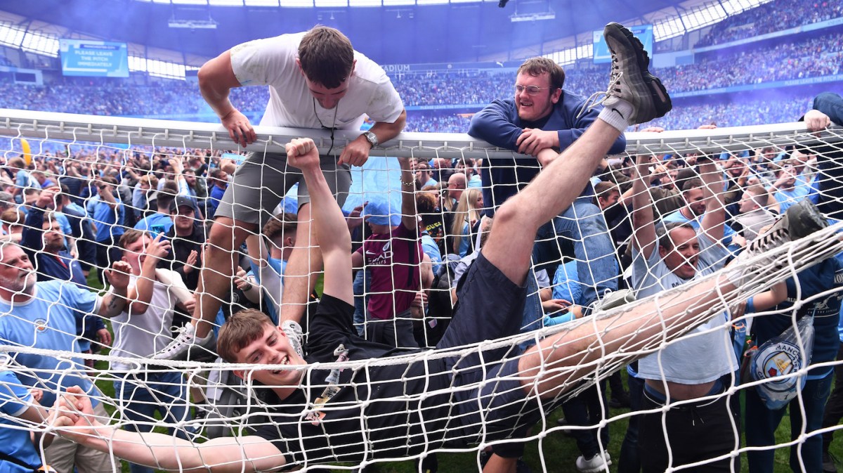 MANCHESTER, ENGLAND - MAY 22: Manchester City fans celebrate winning the Premier League title on the pitch by swinging on the cross bar and lounging on the roof of the net after the Premier League match between Manchester City and Aston Villa at Etihad Stadium on May 22, 2022 in Manchester, England. (Photo by Stu Forster/Getty Images)