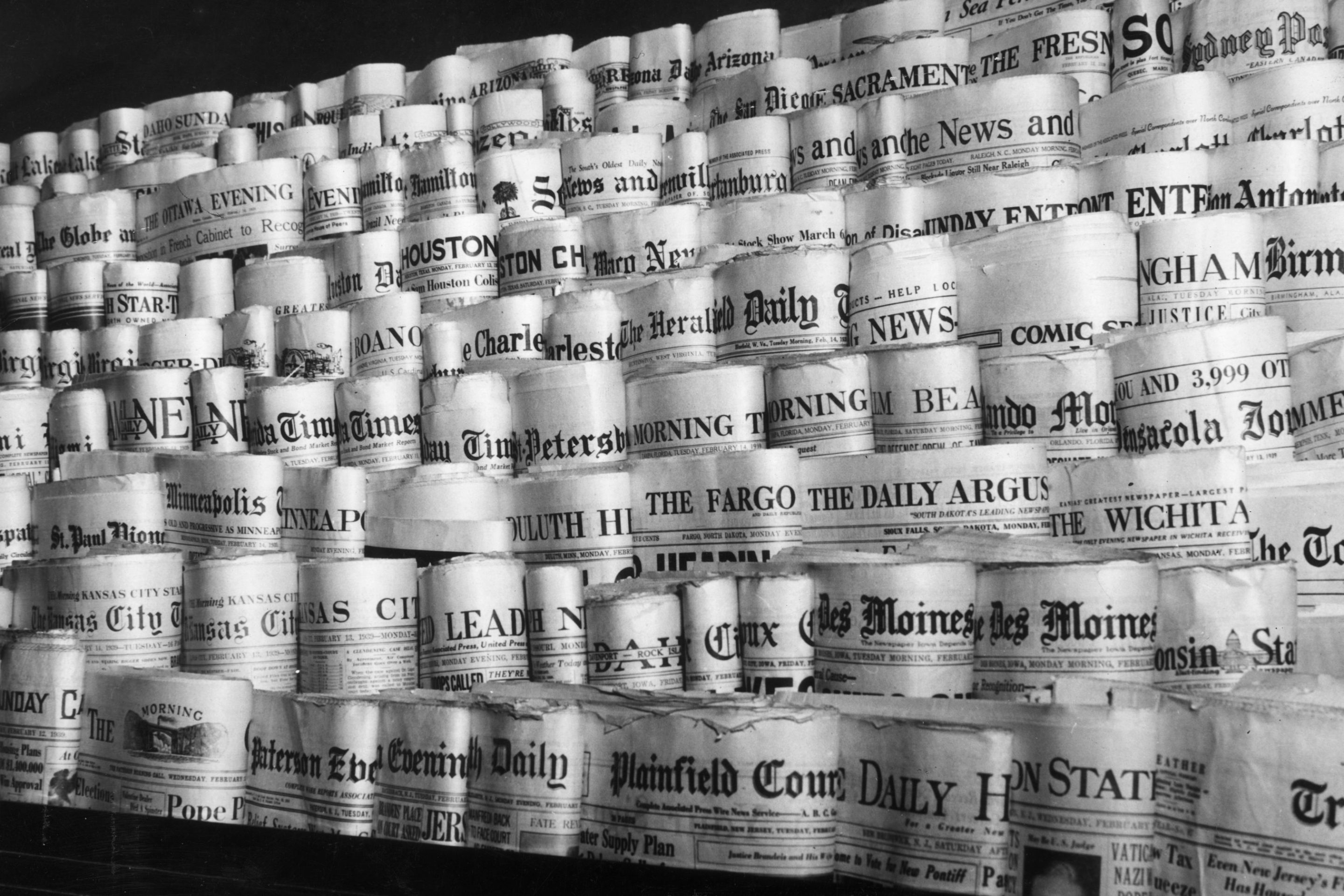 February 1939: View of rows of newspapers from various American cities sitting in the racks of a newsstand, Times Square, New York City.