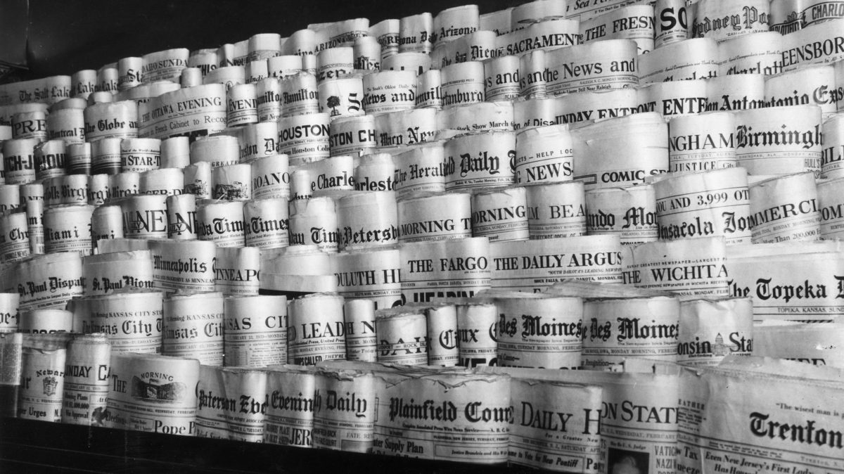 February 1939: View of rows of newspapers from various American cities sitting in the racks of a newsstand, Times Square, New York City.