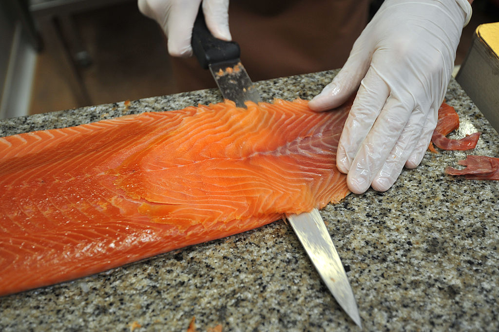 A worker slices smoked salmon on a counter.