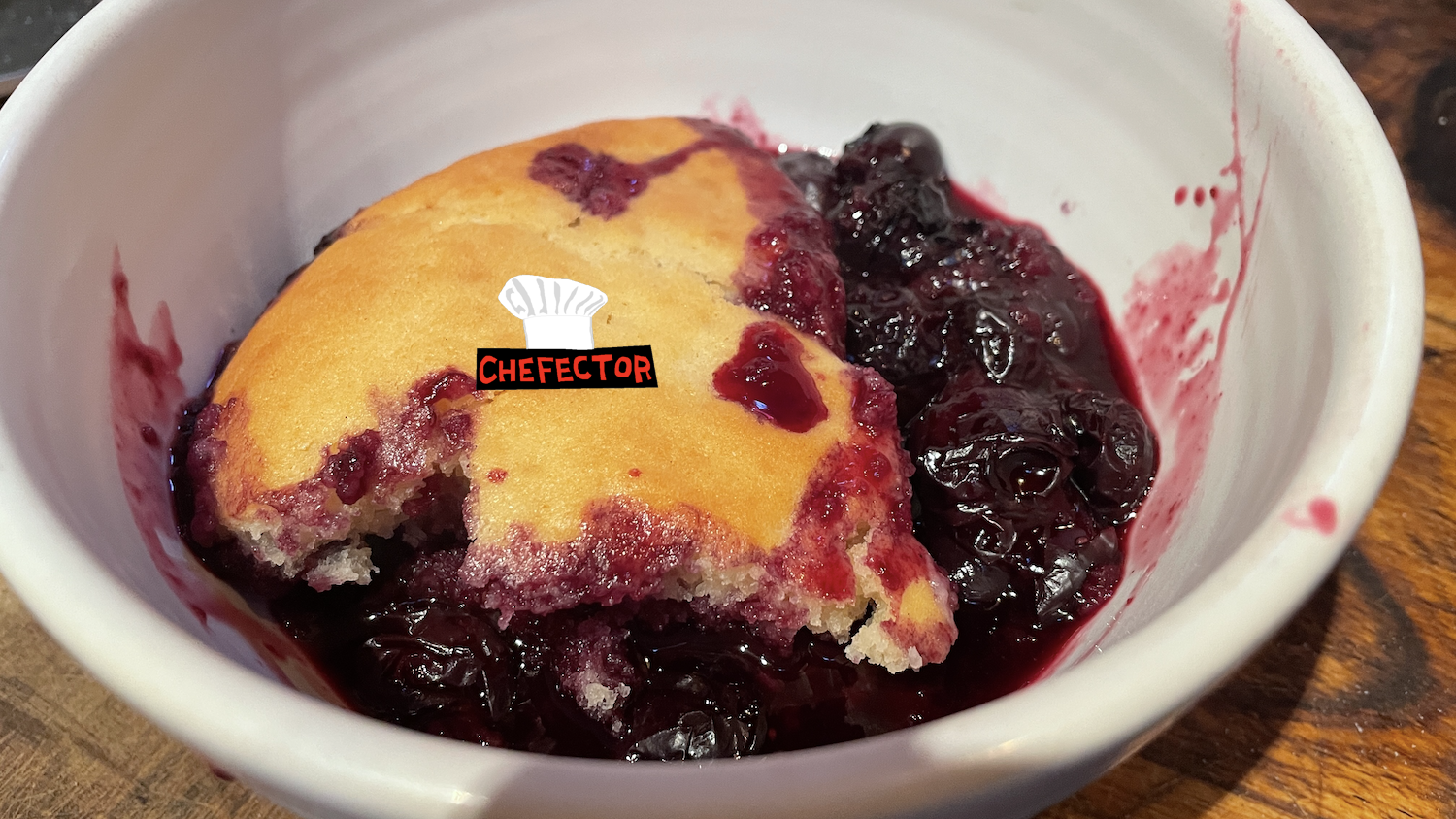 A bowl with some messy blueberry cobbler in it