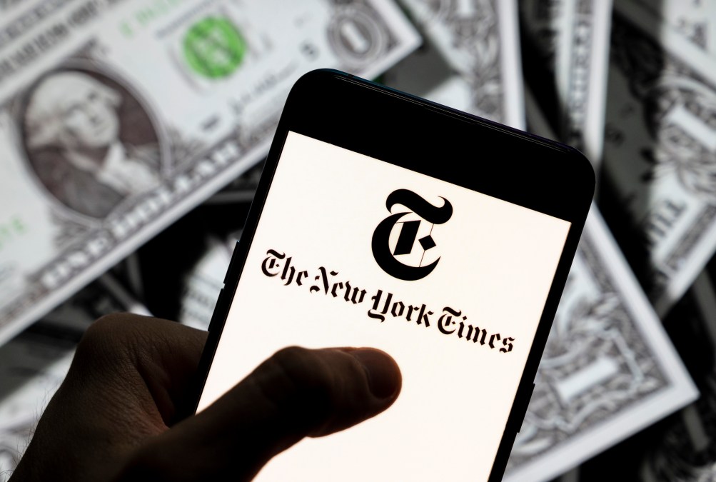 In this photo illustration the American newspaper The New York Times (NYT) logo seen displayed on a smartphone with USD (United States dollar) currency in the background.