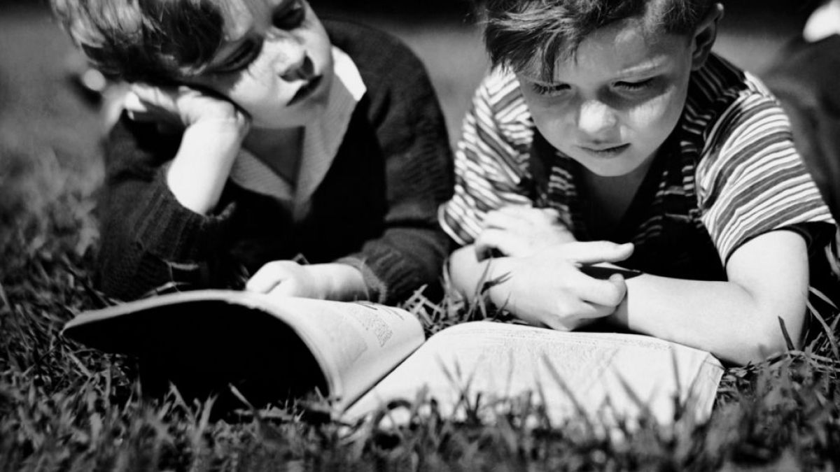 Two boys read a book in the 1950s.