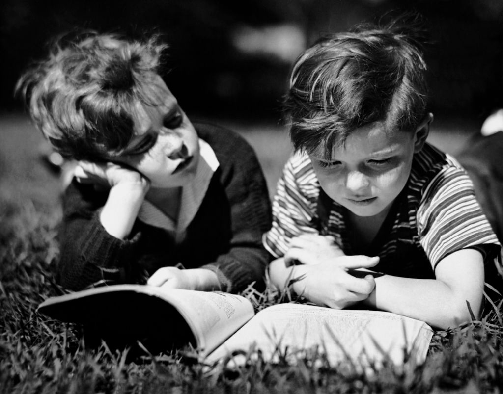 Two boys read a book in the 1950s.