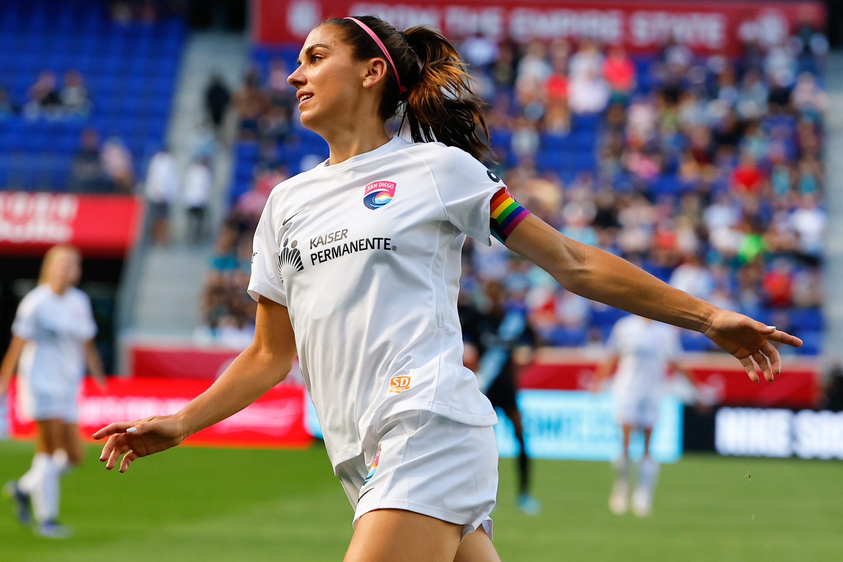 San Diego Wave FC forward Alex Morgan (13) celebrates after scoring during the first half of the NWSL soccer game between NJ/NY Gotham FC and San Diego Wave FC on June 19, 2022 at Red Bull Arena in HArrison, NJ. Her arms are wide open, like an airplane, and she's smiling.