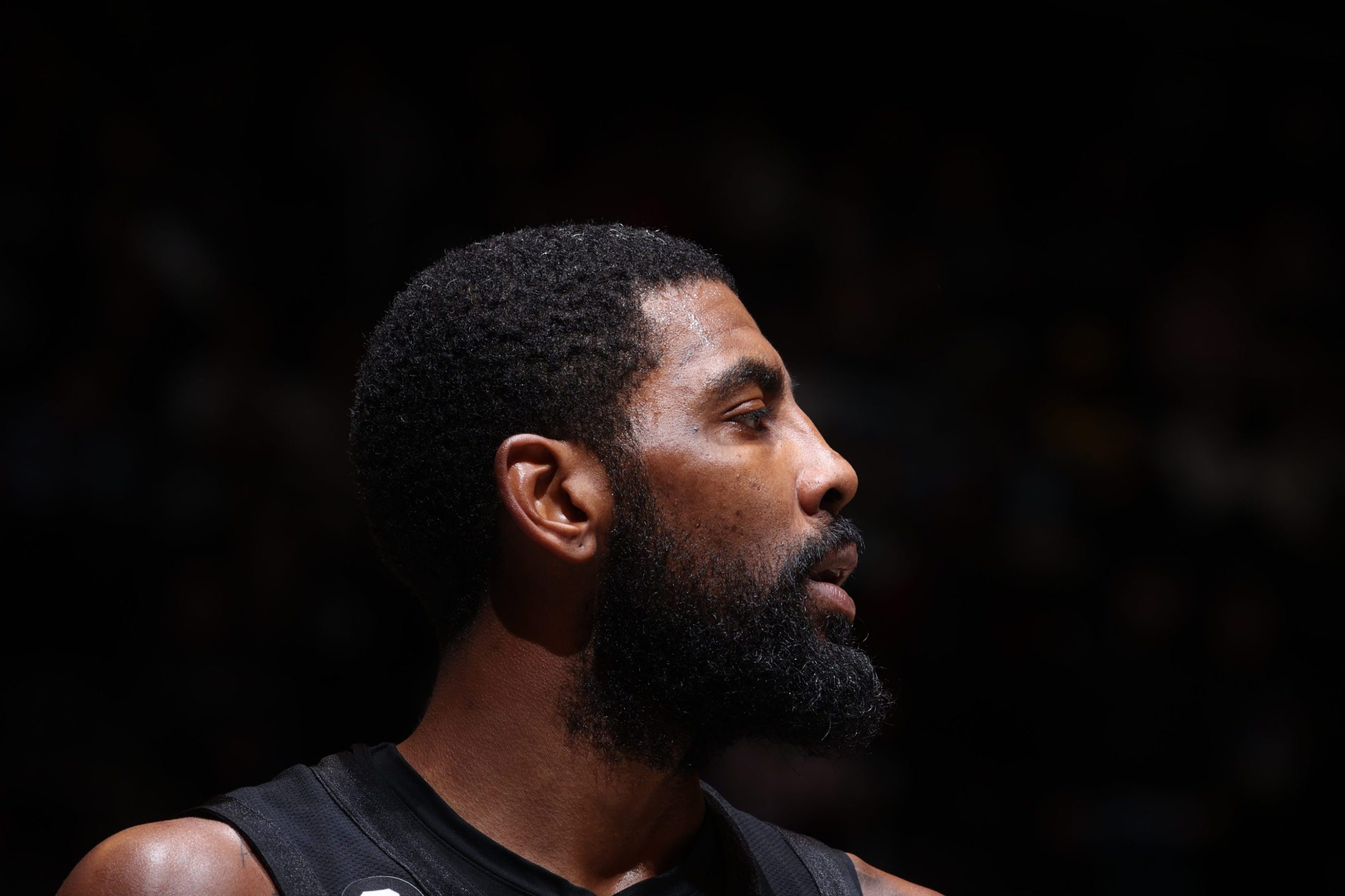 Kyrie Irving #11 of the Brooklyn Nets looks on during the game against the Indiana Pacers on October 31, 2022 at Barclays Center in Brooklyn, New York. The image is zoomed in on his face, which is turned to one side, and behind him is all black.