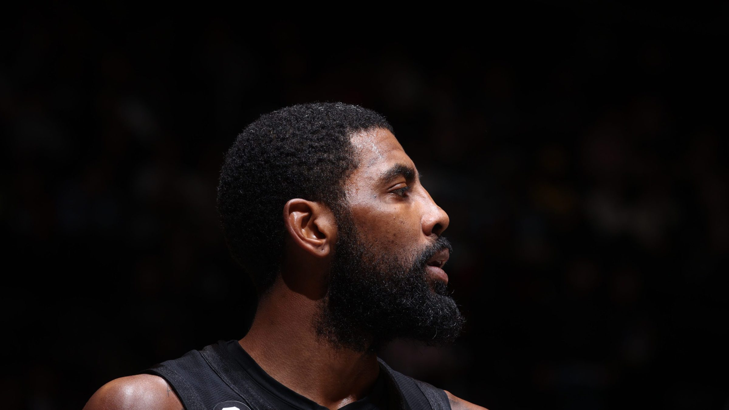 Kyrie Irving #11 of the Brooklyn Nets looks on during the game against the Indiana Pacers on October 31, 2022 at Barclays Center in Brooklyn, New York. The image is zoomed in on his face, which is turned to one side, and behind him is all black.