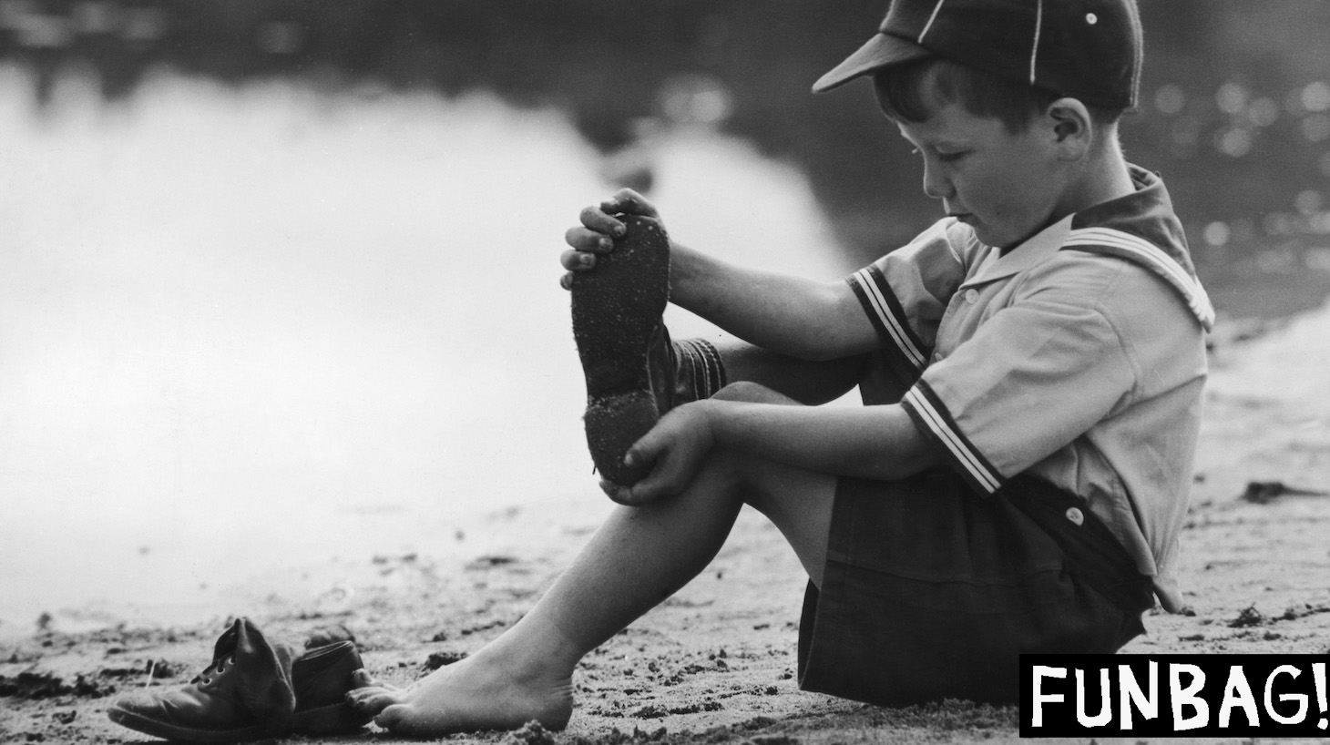 A cub scout takes off his shoes and socks before going for a paddle, circa 1955. (Photo by FPG/Hulton Archive/Getty Images)
