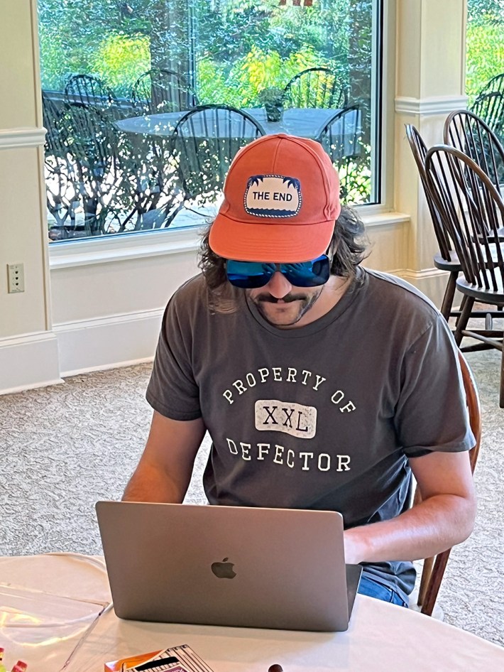 Todd Dipshit, in an orange hat and giant sunglasses, at a computer