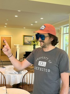 Todd Dipshit, in an orange hat and giant sunglasses, pointing