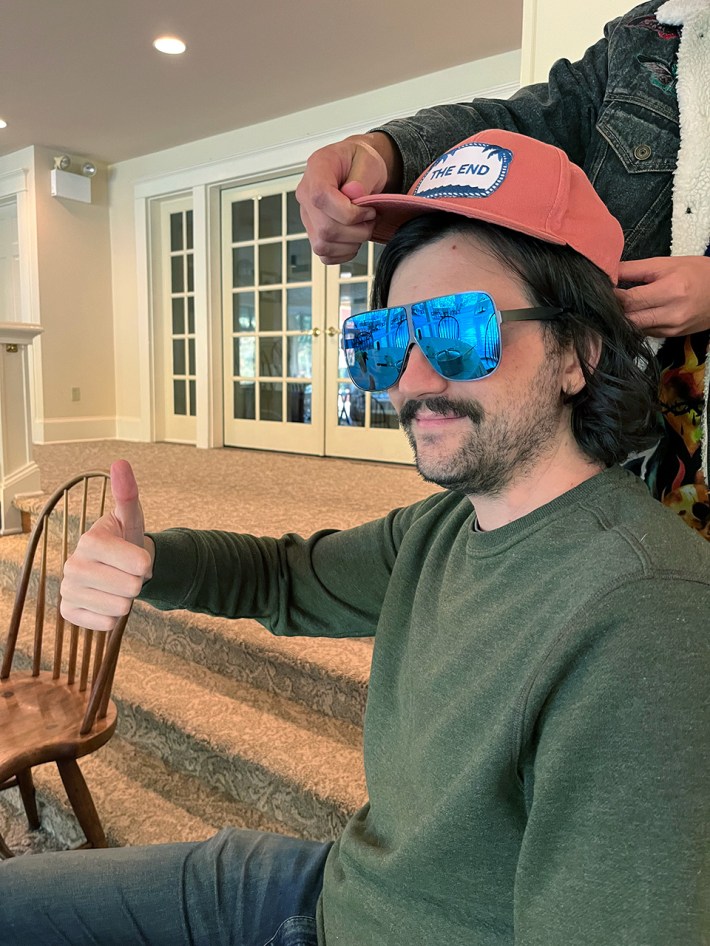 Todd Dipshit, in an orange hat and giant sunglasses, giving a thumbs up