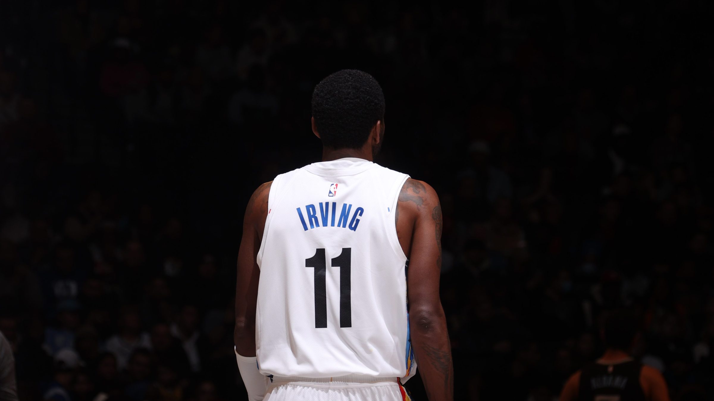 Kyrie Irving #11 of the Brooklyn Nets looks on during the game against the Memphis Grizzlies on November 20, 2022 at Barclays Center in Brooklyn, New York. His back it to the camera, and around him everything else is dark.
