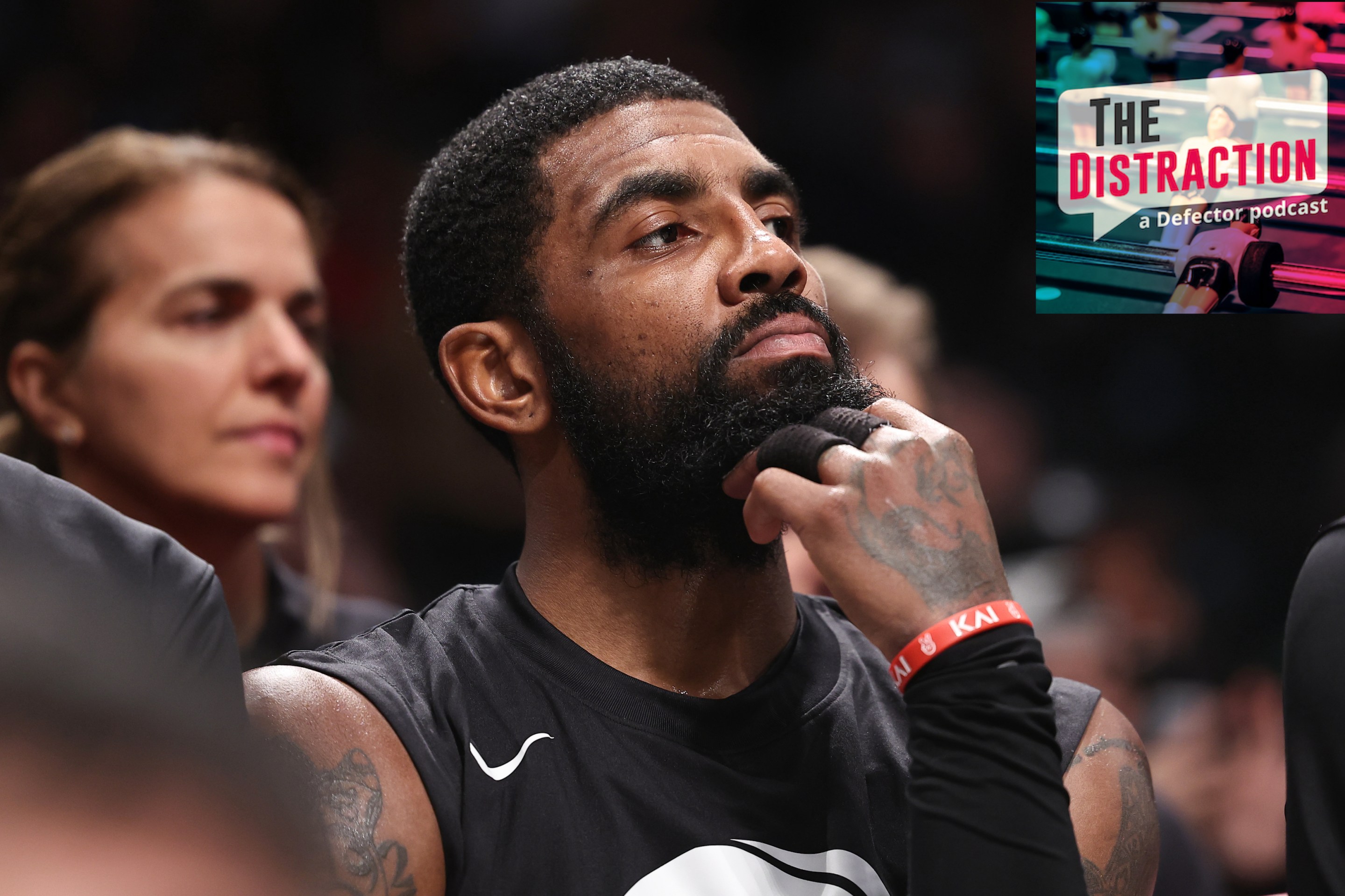 Kyrie Irving on the bench during a Nets game, seemingly staring thoughtfully at The Distraction logo, as if trying to determine its haplogroup.