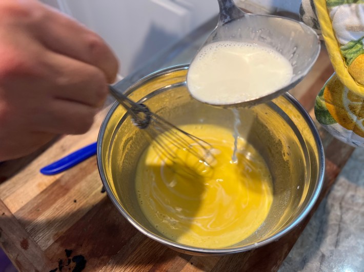 Ladling hot milk into egg yolks and sugar.