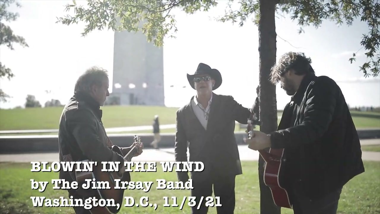 An image of Colts owner Jim Irsay standing in front of the Washington Monument. On each side of him are two rockers with guitars. Irsay is leaning on the tree and singing, yup, Bob Dylan's "Blowin in the Wind." There's text confirming this in the lower left corner, like you used to see in music videos all the time.