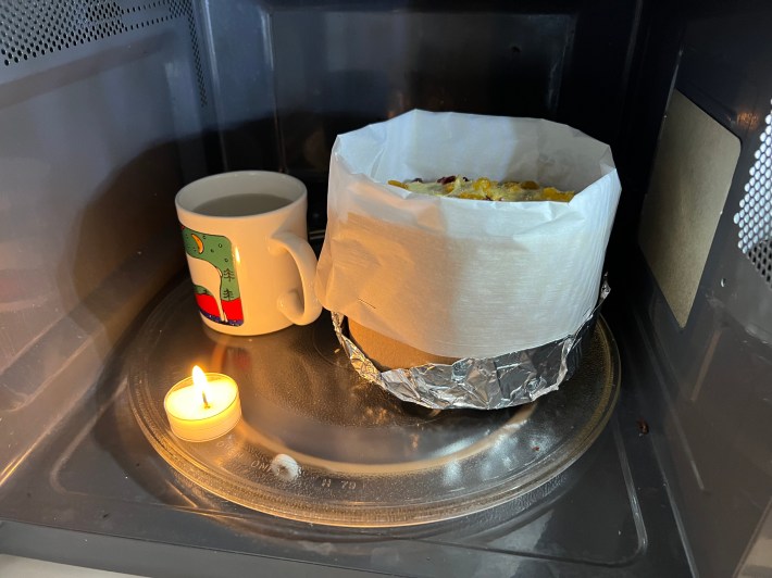 Panettone dough proving in the microwave next to an ignited tea light.