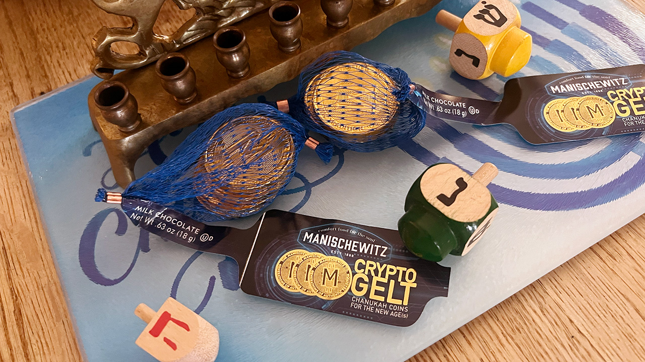 A menorah on a "happy Chanukah" plate. In front of it are dreidels and CRYPTO GELT: Chanukah Coins for the new age.