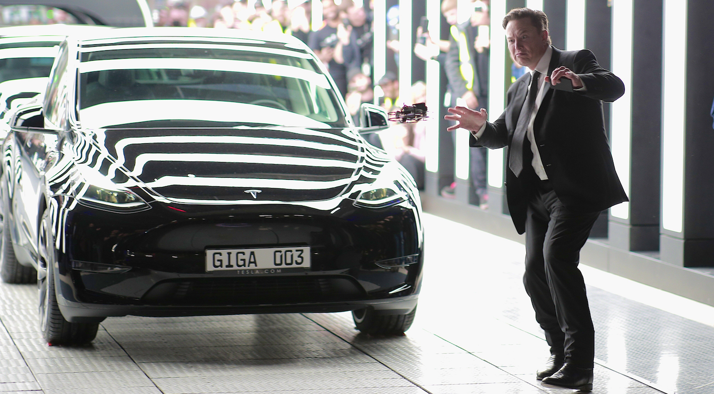 Elon Musk makes a weird face next to a Tesla car