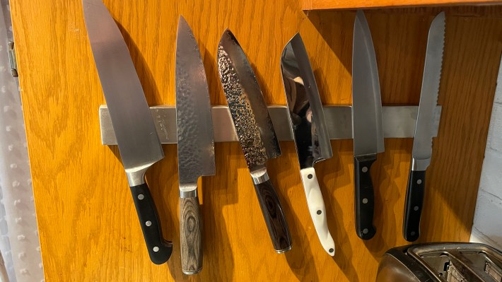 A magnetic knife rack on an ugly wood-paneled wall, with several knives stuck to it