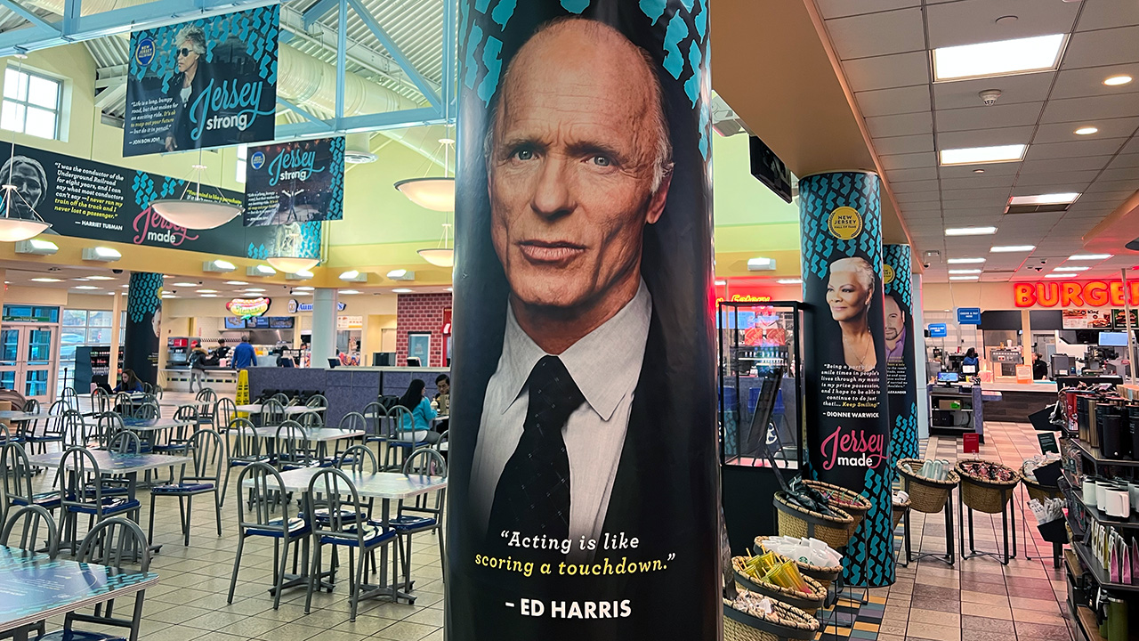 A photo of a New Jersey rest stop. In the foreground is Ed Harris, the actor. He is in a suit. The quote below him is: "Acting is like scoring a touchdown."