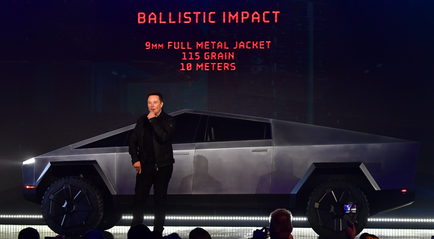 Elon Musk and the Cybertruck, in front of a digital readout bragging about the caliber of gunfire it can withstand for some reason.