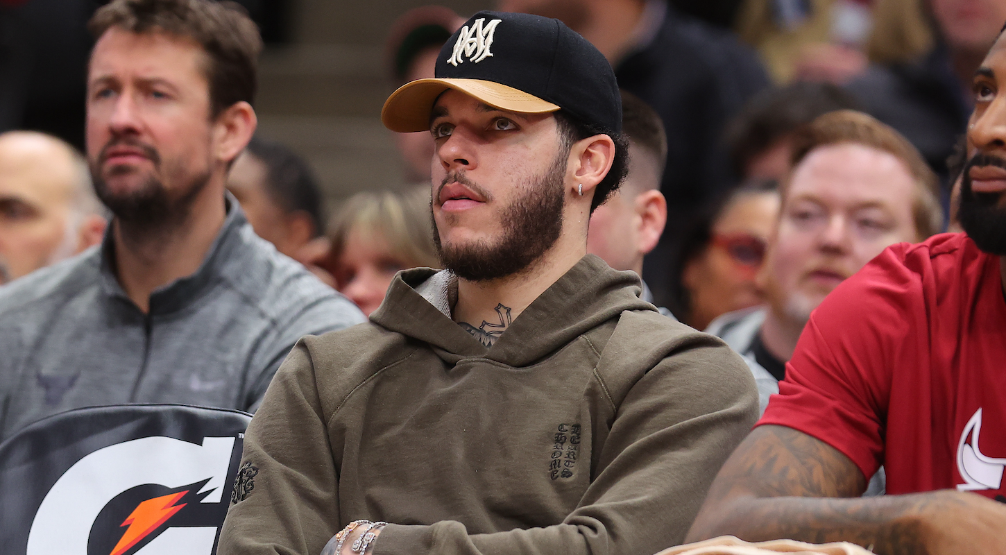 Lonzo Ball watches a Bulls game from courtside, in a hoodie and ball cap.