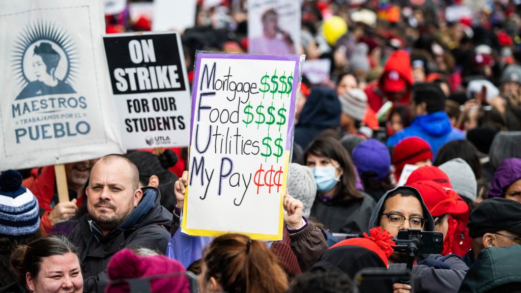 Striking Los Angeles Unified School District employees and their supporters, including teachers, rally outside LAUSD headquarters in Los Angeles on Tuesday, March 21, 2023 during the first day of a three-day strike. At the center of the photo, a person is holding up a sign. It reads: "Mortgage: $$$$ Food: $$$$$ Utilities: $$$$$ My pay: ¢¢¢¢¢¢"