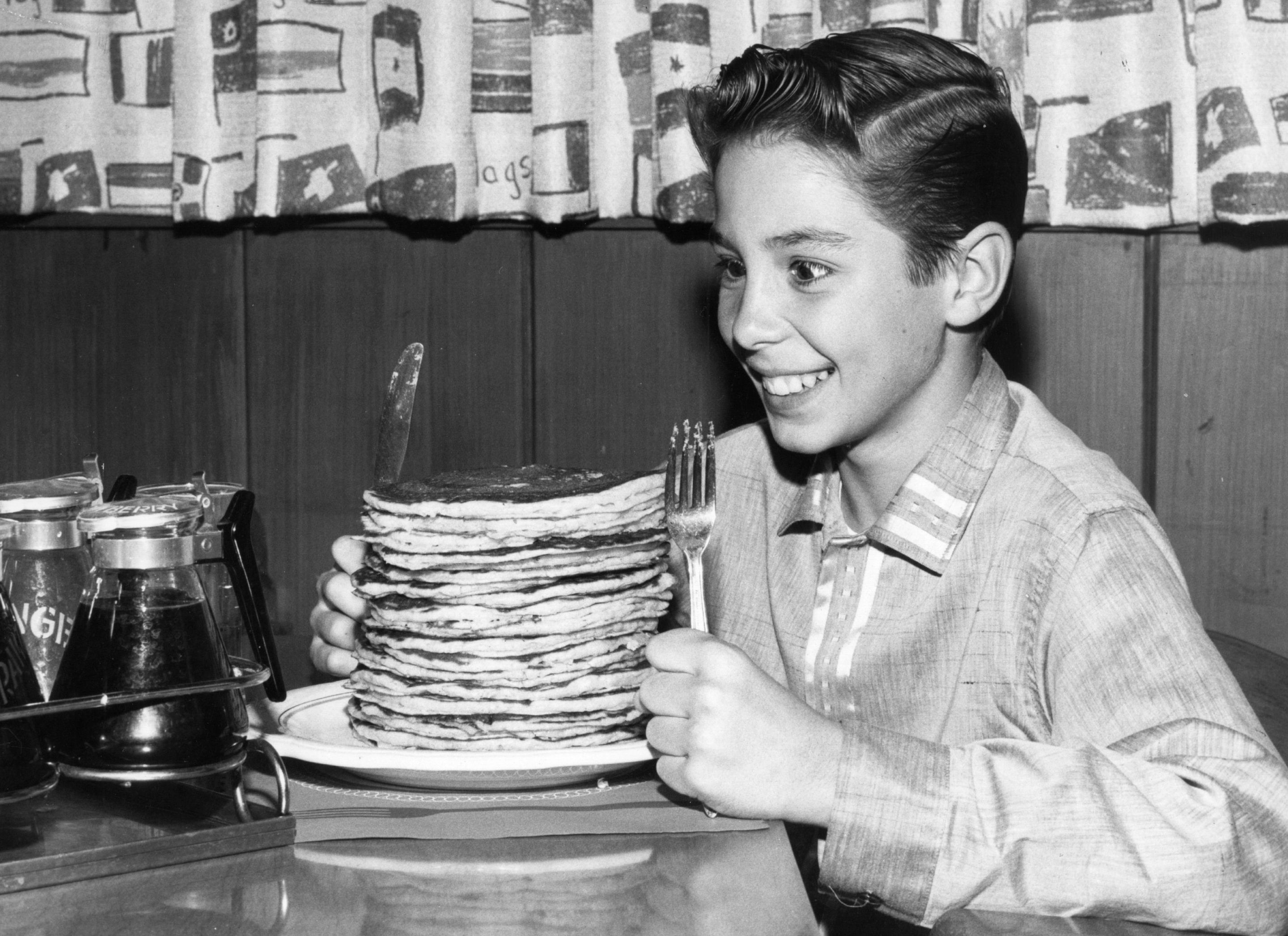 circa 1960: Child actor Johnny Crawford looks forward to eating a pile of pancakes in an International House of Pancakes, a chain of eateries in the USA started in 1958 by Californian brothers Al and Jerome Lapin. (Photo by Keystone Features/Getty Images)