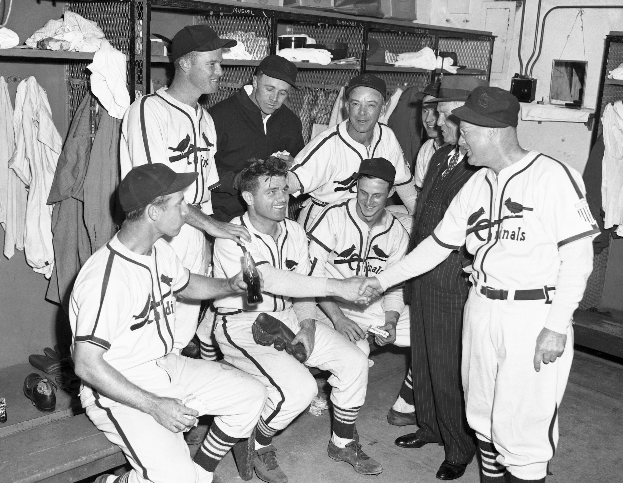 (Original Caption) Cardinals Clinch NL pennant. St. Louis, Missouri: Redbird coach Wares (right) shakes hands with winning pitcher Max Lanier, after the first game of a double header with the Cubs when the Cardinals clinched the National League pennant again this year. (Left to right seated) Chuck Klein; Lanier; Stan Musial; (left to right standing) George Munger; Ernie White; manager Billy Southworth; Danny Litwhiler; owner Sam Breadon, and Wares.