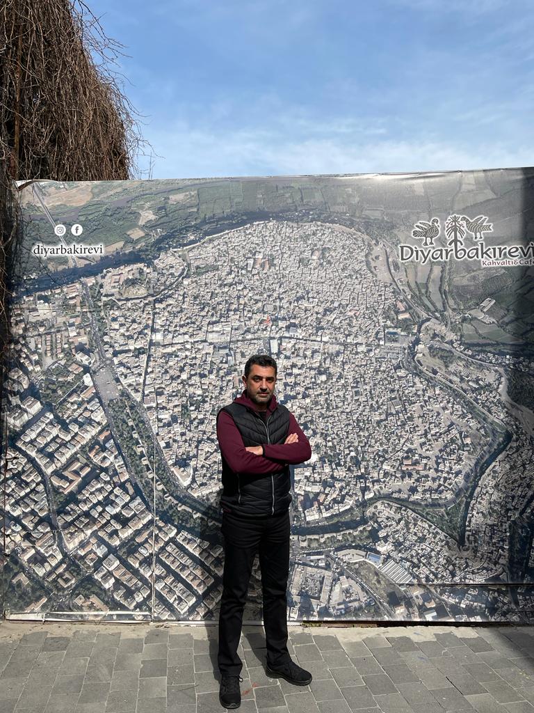 Merthan stands beside a map of Sur before the war
