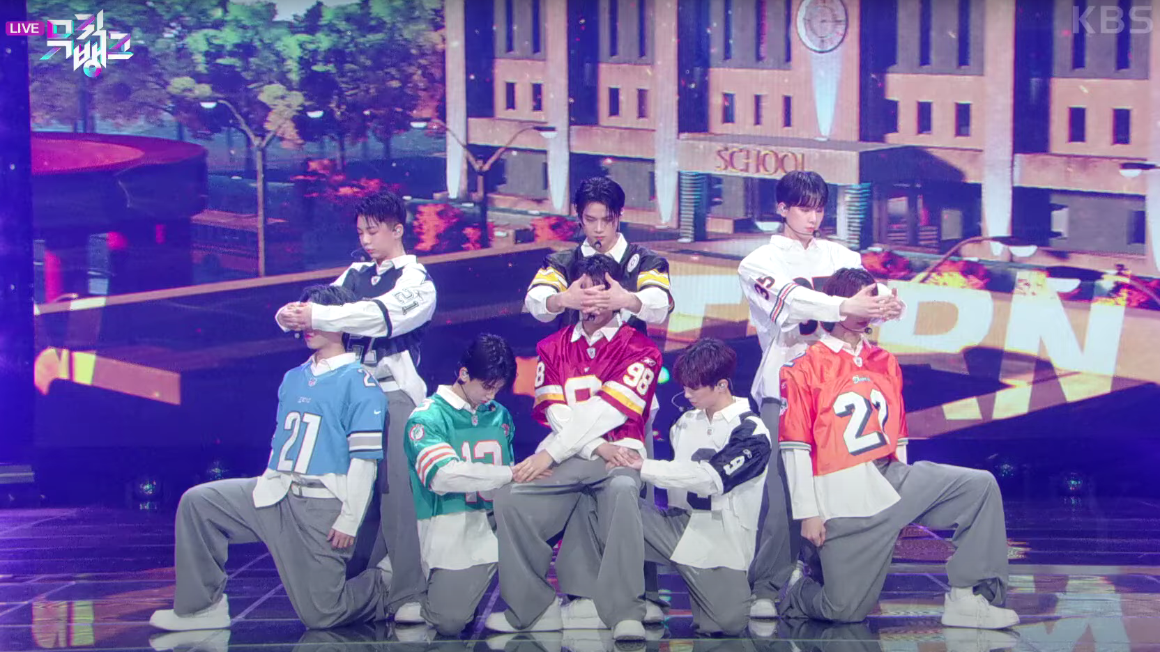 A photo of the K-Pop group 8TURN as they are about to perform on the TV show Music Bank. Each is wearing a vintage NFL jersey.