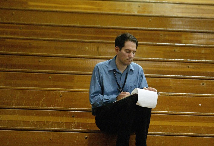 Jon Solomon writes in a note book in the stands in an empty wooden bleachers
