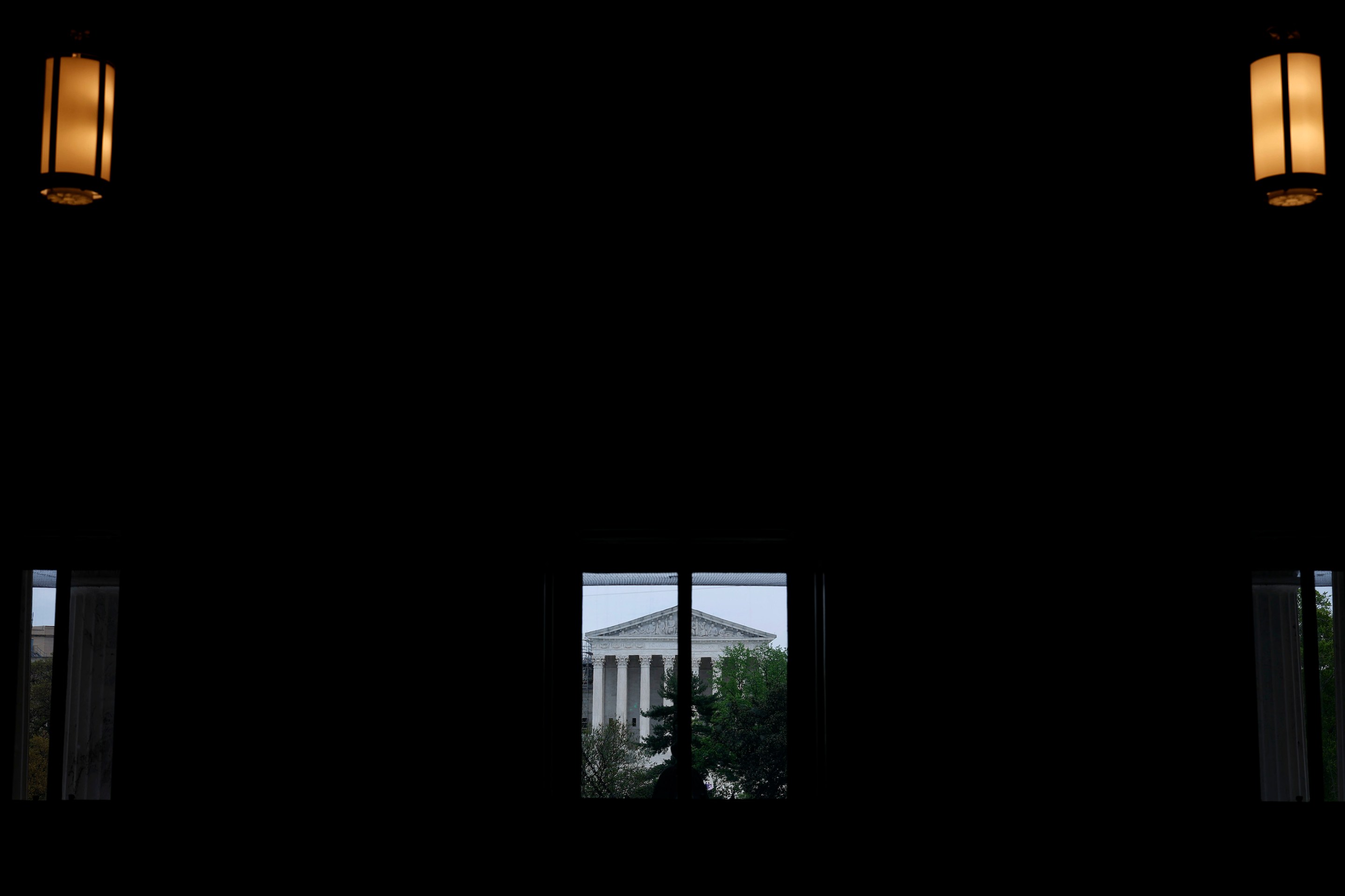 The United States Supreme Court building seen from a distance, through a window, from inside a darkened room.