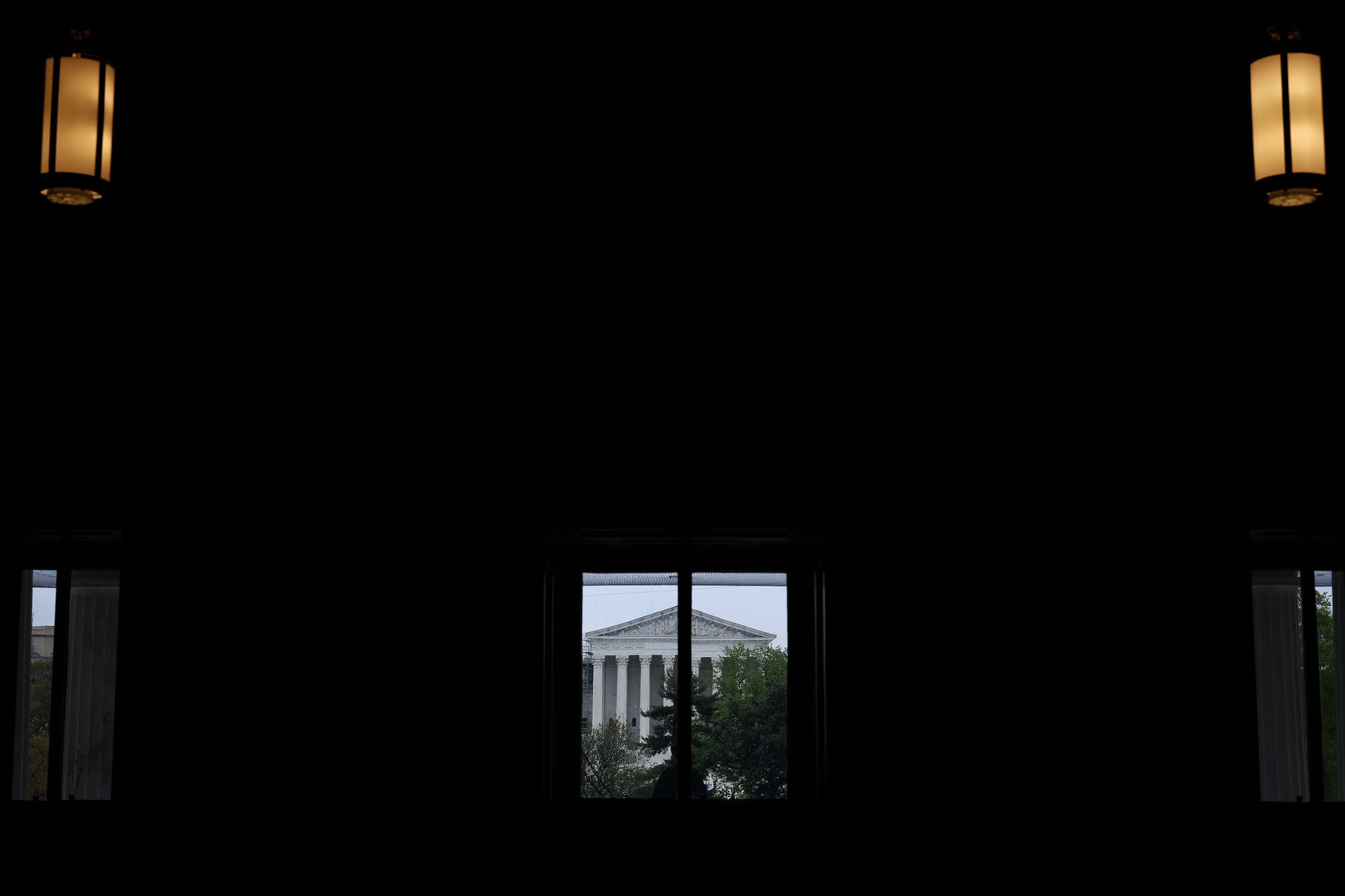 The United States Supreme Court building seen from a distance, through a window, from inside a darkened room.