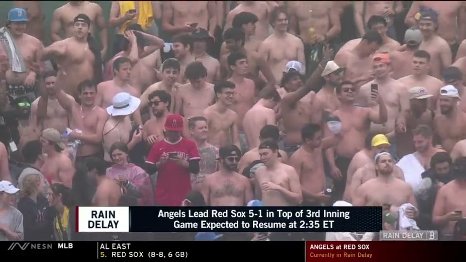 A bunch of shirtless Red Sox fans in the stands at Fenway Park, with one Angels fan (not shirtless) texting in the middle of it all