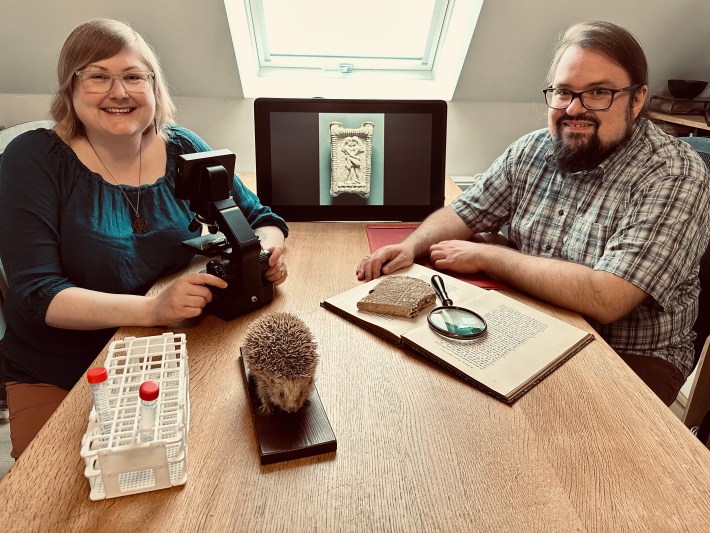 A photo of the researchers Sophie Lund Rasmussen and Troels Pank Arboll posing with a hedgehog and an image of an ancient kiss—the objects of their research