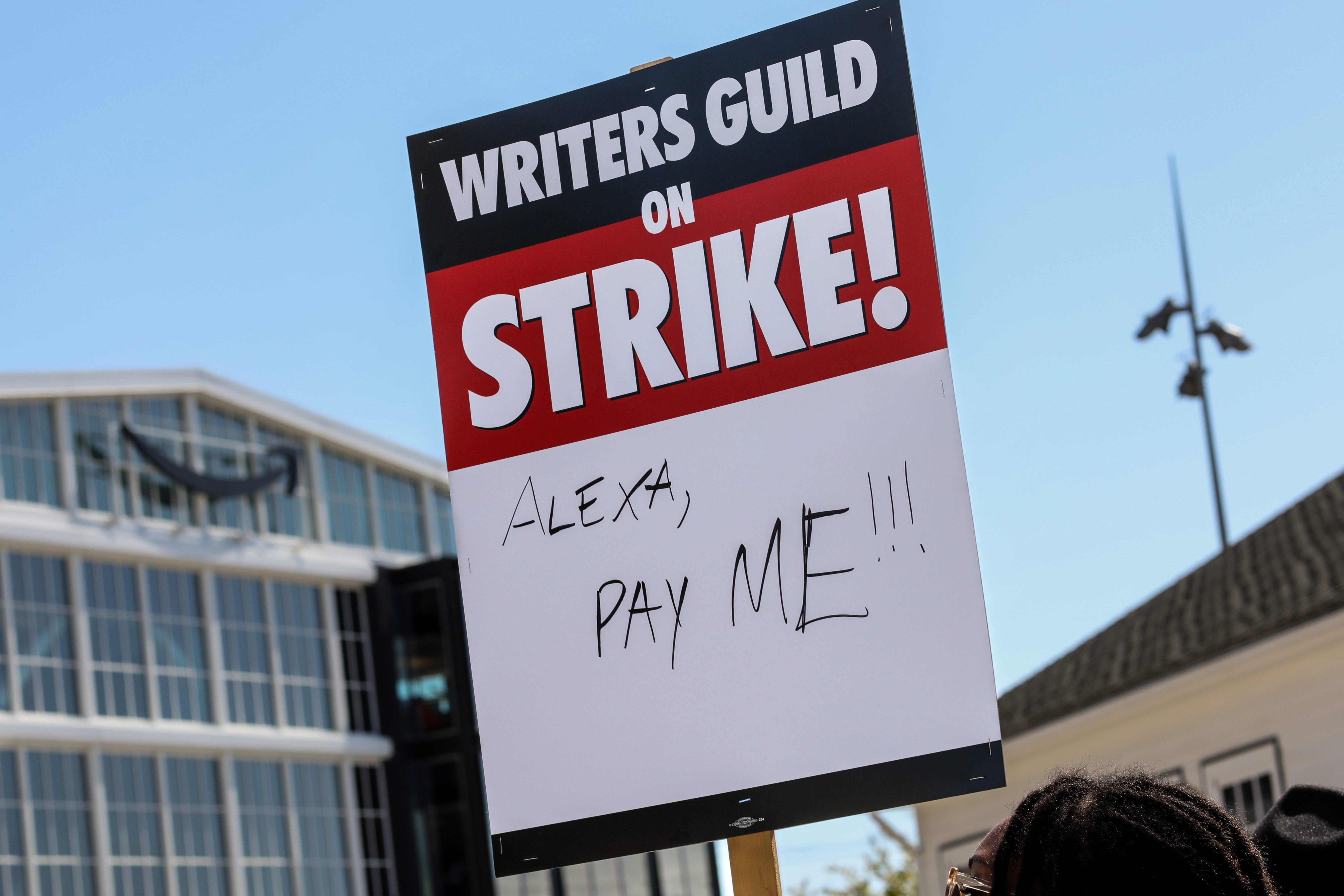 A supporter of the Writers Guild of America pickets holding a sign that reads, "Alexa, pay me!," in front of Culver Studios, home of Amazon Studios, on Tuesday, May 2, 2023, as the WGA strike began, in Culver City, CA.