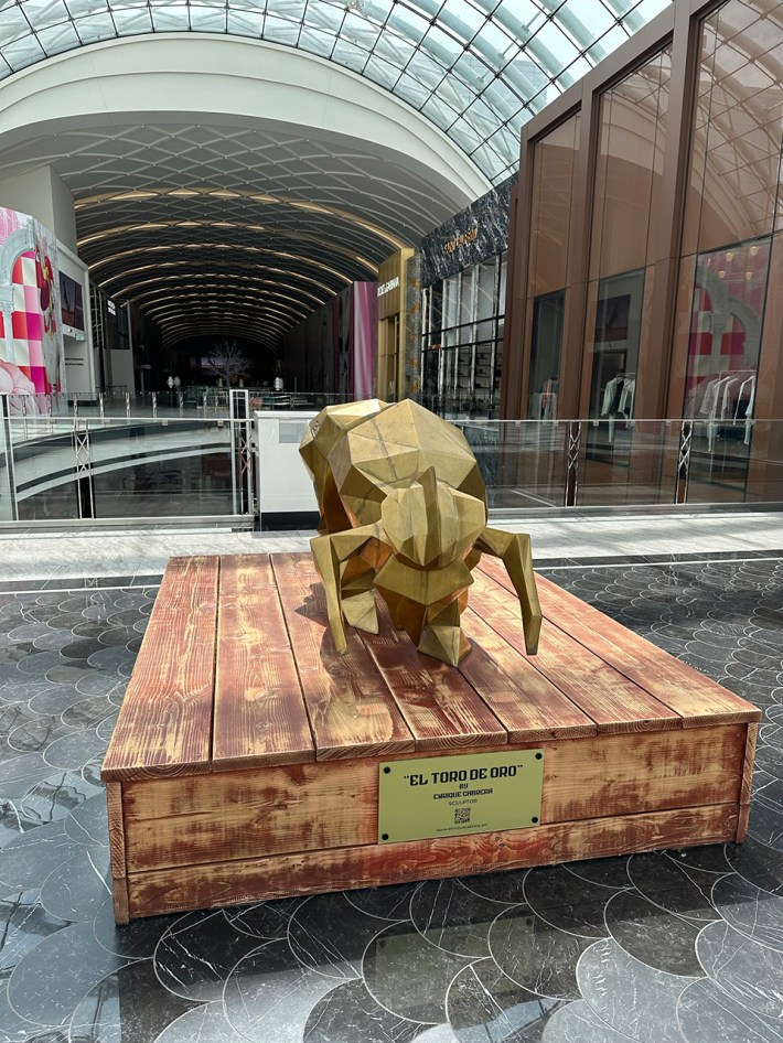 A gold bull sculpture called EL TORO DE ORO on a wooden stand. THe artist is Enrique Cabrera.