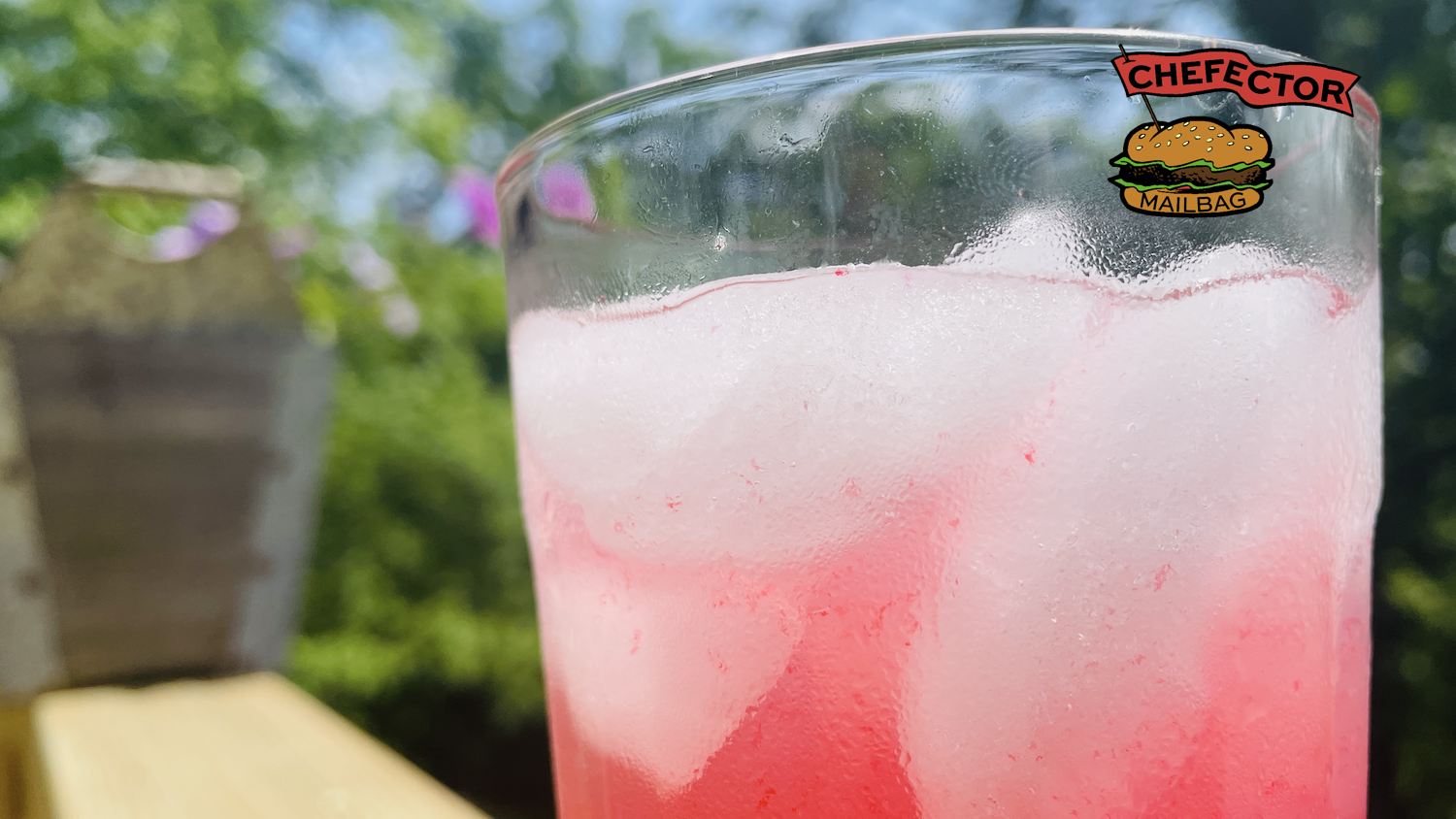 A glass of pink lemonade, outside with flowers in the background.