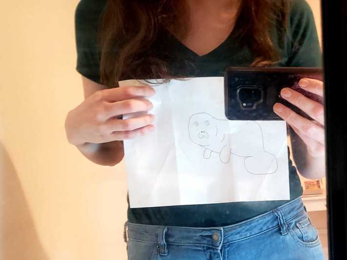 Lauren holding a drawing of Devin in front of her shirt in the mirror.
