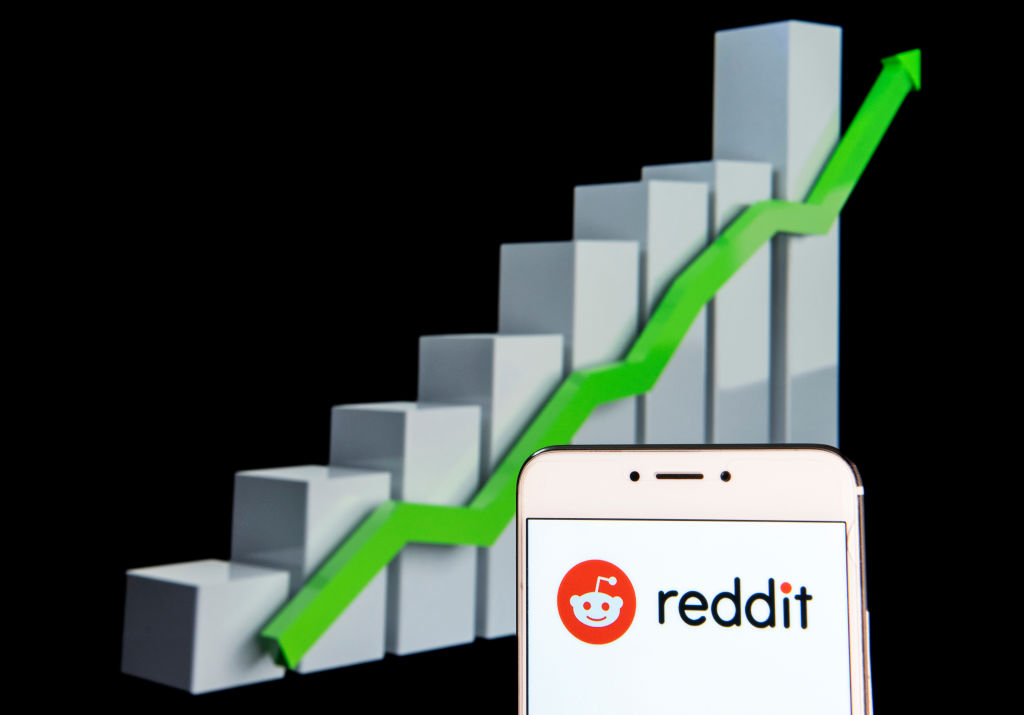 Reddit logo is seen on an android mobile device with an ascent growth chart in the background.