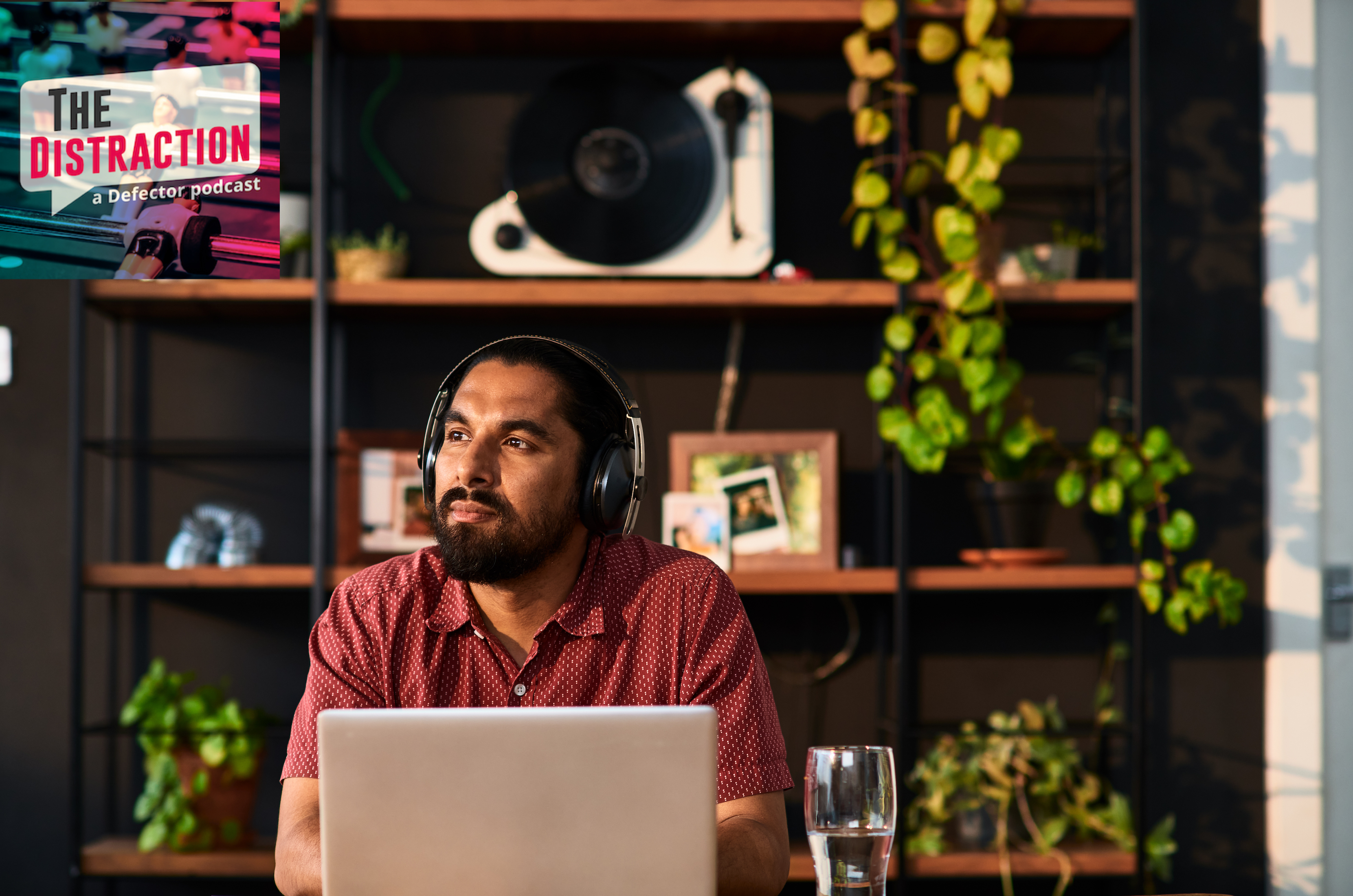 A stock photo of a man in his thirties sitting at a computer with headphones on, presumably thinking about podcasts.