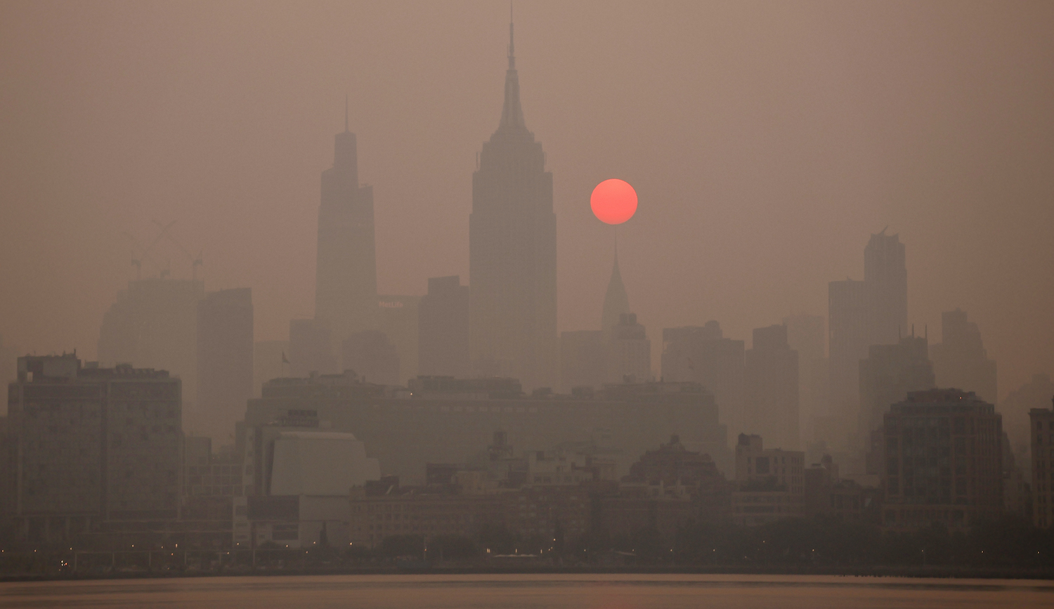 JERSEY CITY, NJ - JUNE 8: The sun is shrouded as it rises in a smokey sky behind the Empire State Building, Chrysler Building and One Vanderbilt in New York City on June 8, 2023, as seen from Jersey City, New Jersey. (Photo by Gary Hershorn/Getty Images)
