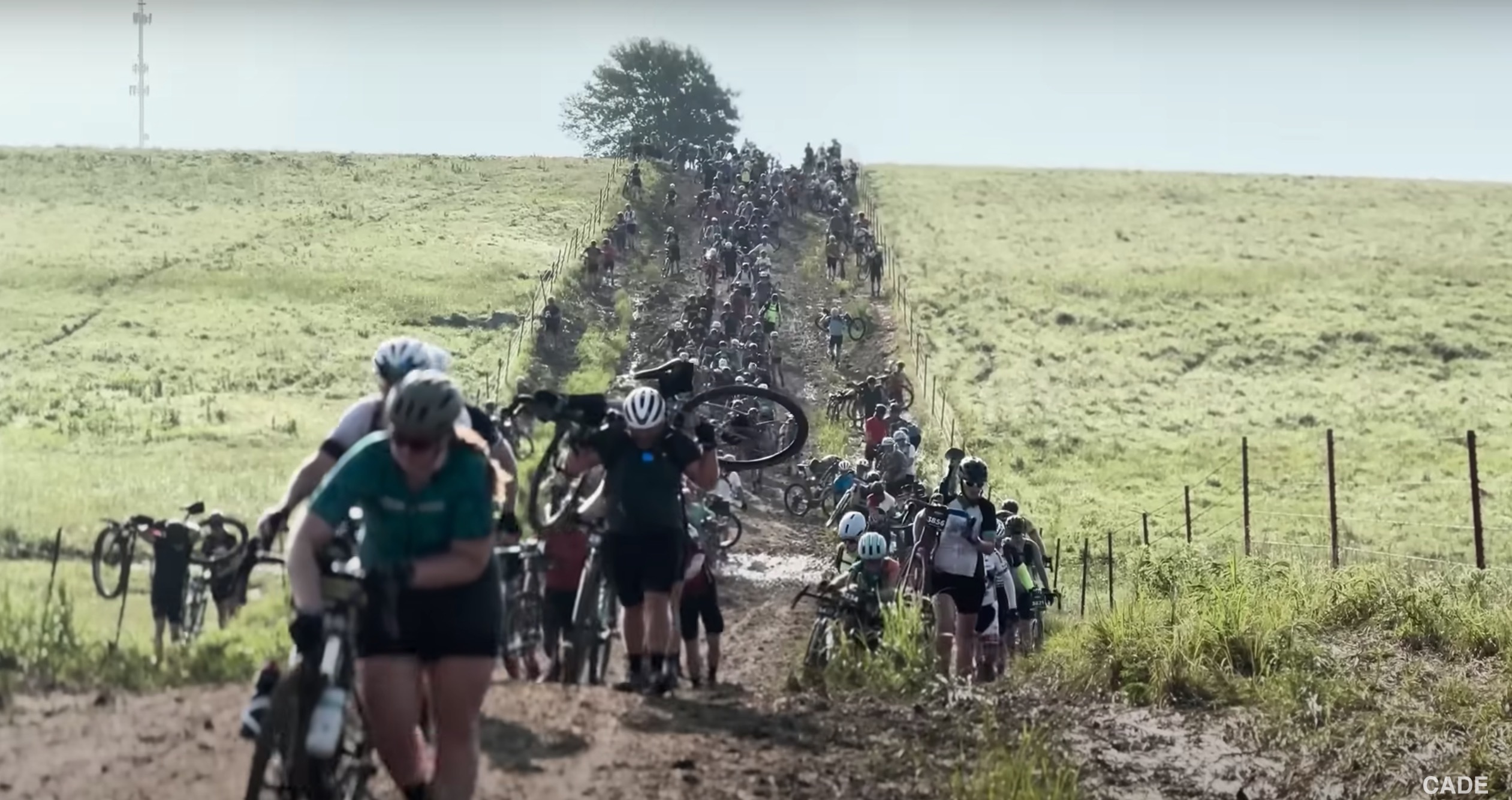 Cyclists walk their bikes through a muddy portion of the 2023 Unbound gravel race
