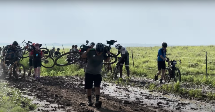 Cyclists carry their bikes through a horribly muddy section of Unbound 2023.