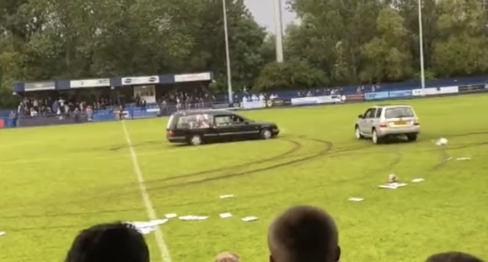 A hearse and another vehicle drive in circles on a soccer field