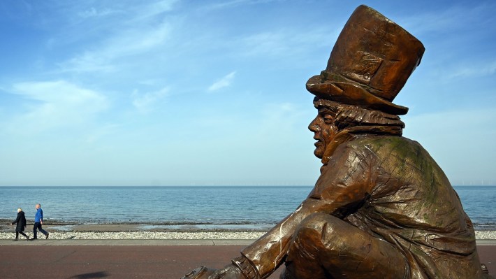 People walk past the Mad Hatter statue on the promenade in LLandudno, north Wales on March 23, 2020.