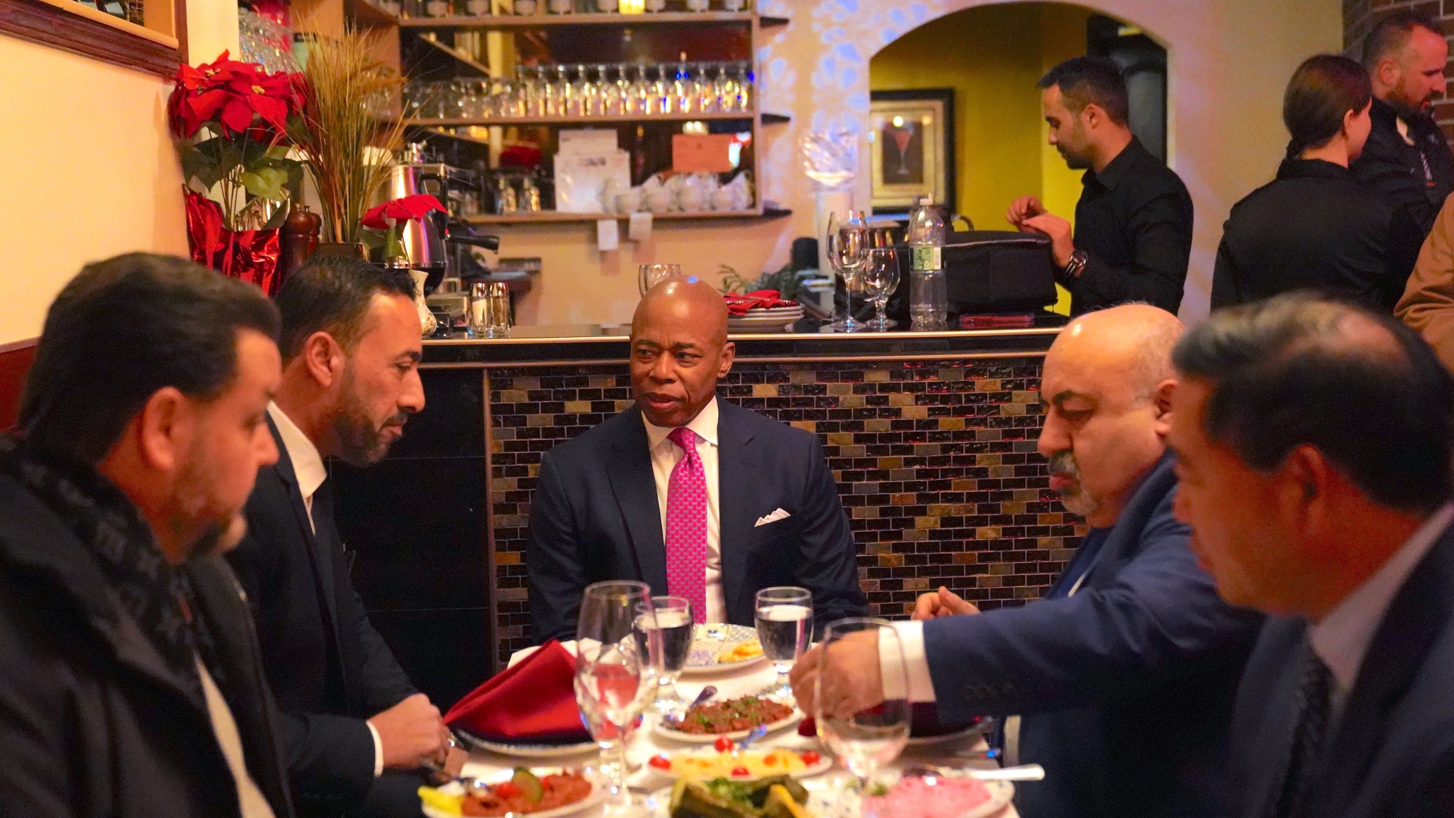 New York City Mayor Eric Adams sitting at a literal table with some restauranteurs at the Manhattan restaurant Ali Baba. This is not the same as the figurative "table of success" at which his haters are his waiters.