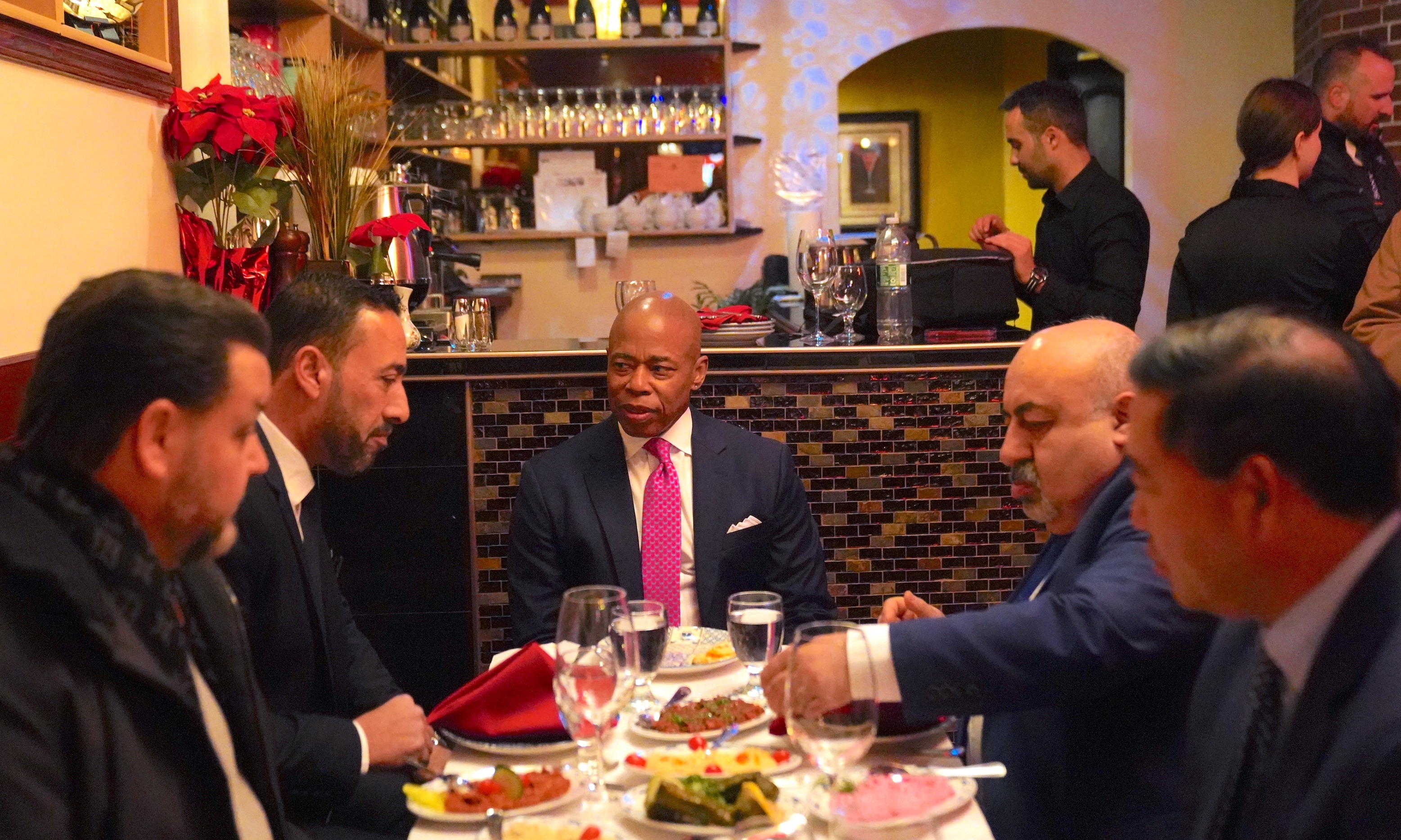 New York City Mayor Eric Adams sitting at a literal table with some restauranteurs at the Manhattan restaurant Ali Baba. This is not the same as the figurative "table of success" at which his haters are his waiters.