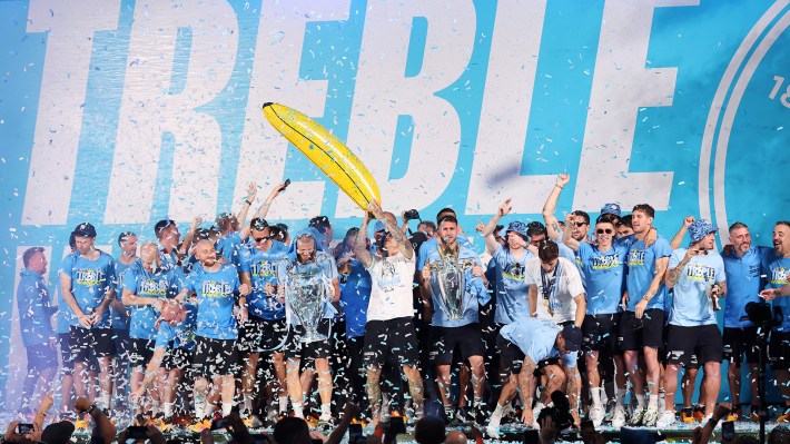 A general view as players of Manchester City celebrate in front the "Treble" banner on stage in St Peter's Square as Erling Haaland of Manchester City celebrates with the UEFA Champions League Trophy, Aymeric Laporte celebrates with the Premier League Trophy and Ruben Dias celebrates with the FA Cup Trophy during the Manchester City trophy parade on June 12, 2023 in Manchester, England.